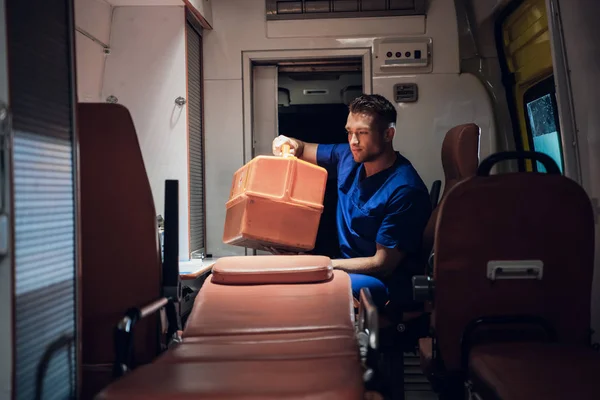 Санитар сидит в машине скорой помощи и упаковывает медицинскую сумку. — стоковое фото