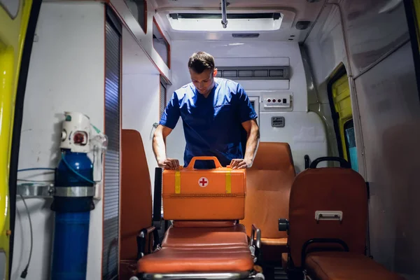 Молодой врач в форме упаковывает медицинскую сумку в машину скорой помощи — стоковое фото