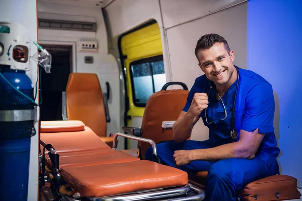 Young corpsman in uniform sits in the ambulance car and smiles — Stockfoto