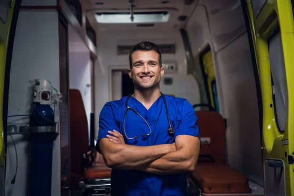 Un forense sonriente con uniforme se para en el coche de la ambulancia —  Fotos de Stock
