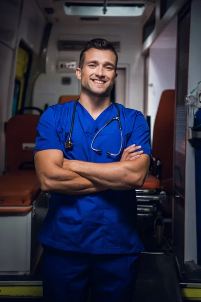Médico en uniforme médico azul se para y mira a la cámara con sonrisa —  Fotos de Stock