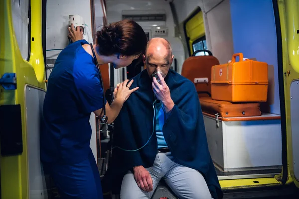 Enfermera joven en uniforme se pone de pie con el hombre que se sienta en la máscara de oxígeno en manta —  Fotos de Stock