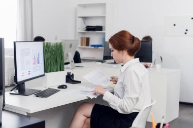 Young woman sits at a table and works with documents in the office