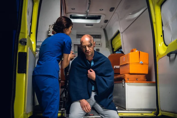 Enfermera pone máscara de oxígeno en el hombre sentado en manta en el coche de la ambulancia — Foto de Stock