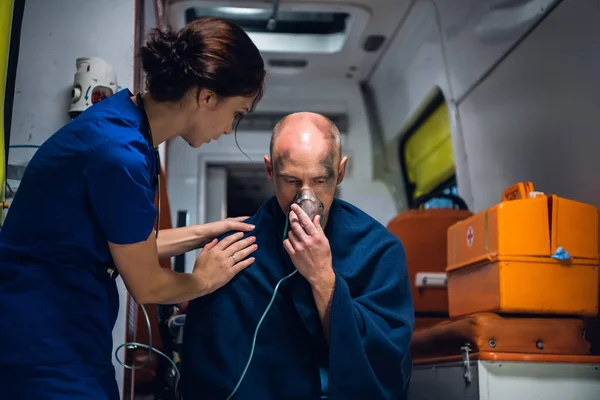 Доктор стоит рядом с человеком, который сидит в кислородной маске в одеяле — стоковое фото