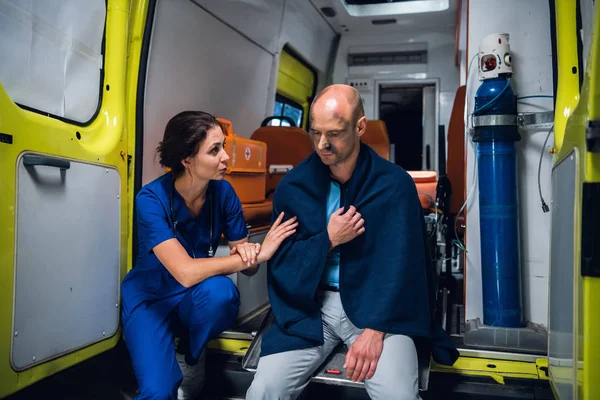 Медсестра сидит и говорит дружелюбно с мужчиной в одеяле в машине скорой помощи — стоковое фото