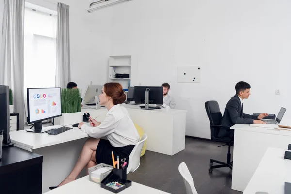 Mężczyzna w garniturach i kobieta w spódnicy siadają przy stolikach i pracują z laptopami w biurze — Zdjęcie stockowe