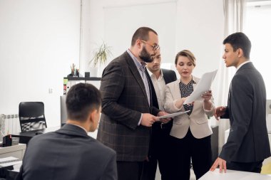 Colleages stand with documents in their hands and woman tells something to her chief