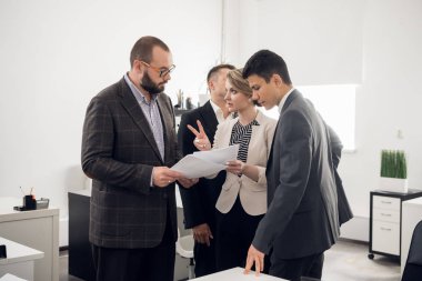 Workers in suits stand and discuss the documents with their chief