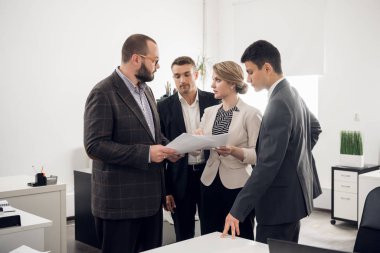 Group of people stand with the documents and look at their chief in the office