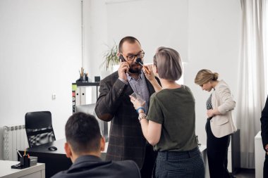 Woman puts a powder on mans face, he stand and talks on phone