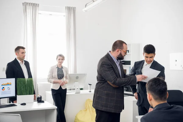 Arbeitstag im Büro, Chef zeigt einem Mann Dokumente, andere Kollegen stehen um sie herum im Büro — Stockfoto