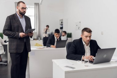 Chief stands over the man in suit sitting at a table and working on a laptop