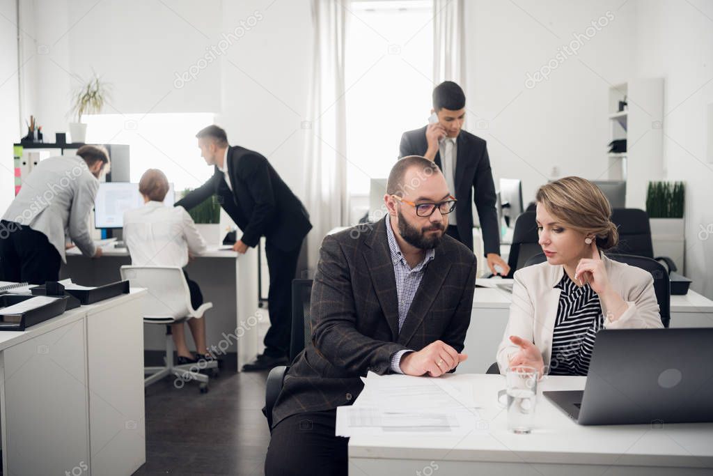 Office workers talk about something, man talks on phone, other three work at a table on backgorund