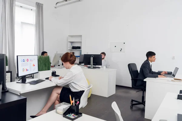 Men and young woman sit at a tables and work with laptops in the office