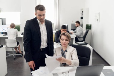 People work in the office, man in stand over the woman and look at documents