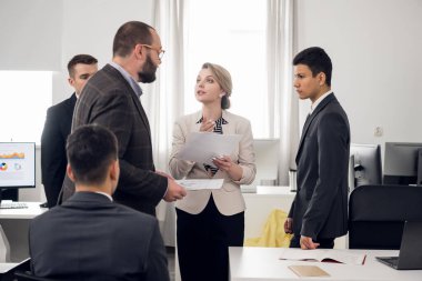 Woman with documents in her hands talk agressively with her chief, coworkers stand around them