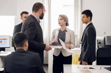 Lady in suit with documents in her hands look agressively with her chief, coworkers stand around them