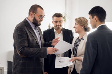 Ofis çalışanları bir araya gelip belgeleri tartışır.