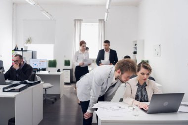Erkekler bir şeyler tartışıyor. Adam meslektaşına yardım ediyor. Adam dizüstü bilgisayarla aynı masada oturuyor.