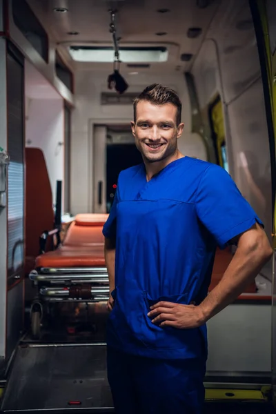 El forense feliz se para con una sonrisa sobre el coche de la ambulancia en el fondo —  Fotos de Stock