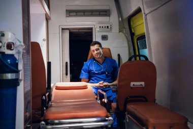 Sıhhiyeci ambulans vagonunda oturur ve gülümser.
