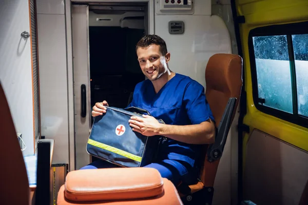 Tıbbi üniformalı bir adam ambulans vagonunda oturur ve sağlık çantası taşır. — Stok fotoğraf