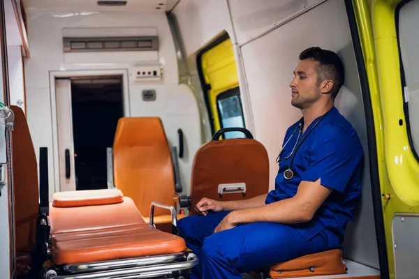 Санитар в медицинской форме сидит в машине скорой помощи. — стоковое фото