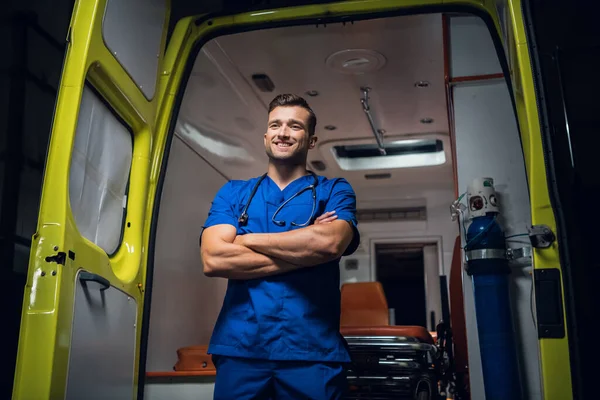 El doctor en uniforme se para y sonríe en el coche de la ambulancia —  Fotos de Stock