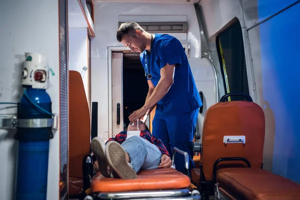 Doctor in medical uniform puts oxygen mask on woman lying on stretcher in the ambulance car — 图库照片