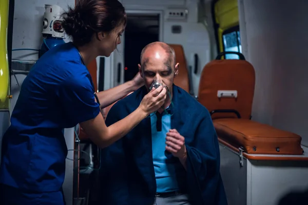 Медсестра надевает кислородную маску на человека, сидящего в одеяле — стоковое фото