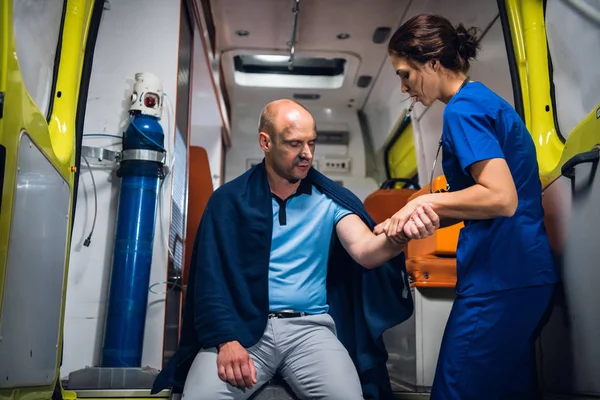 Мужчина сидит в одеяле, доктор в медицинской форме держит руку в машине скорой помощи — стоковое фото