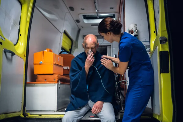 Doctor en uniforme está con el hombre que se sienta en la máscara de oxígeno en la manta —  Fotos de Stock