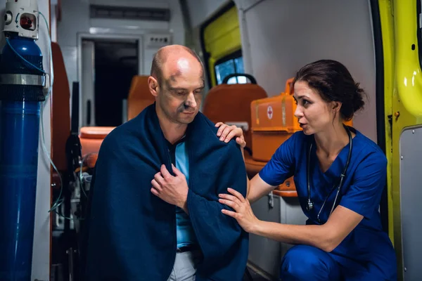 Медсестра говорит дружелюбно с мужчиной в одеяле в машине скорой помощи — стоковое фото