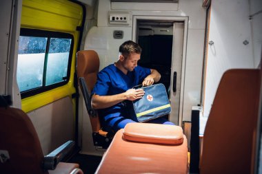 Üniformalı sıhhiyeci ambulans vagonunda oturur ve sağlık çantasını tutar.