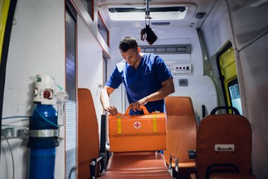Üniformalı genç sağlık görevlileri ambulans arabasına tıbbi çanta koyuyor.