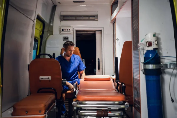 Молодой врач в форме сидит в машине скорой помощи — стоковое фото