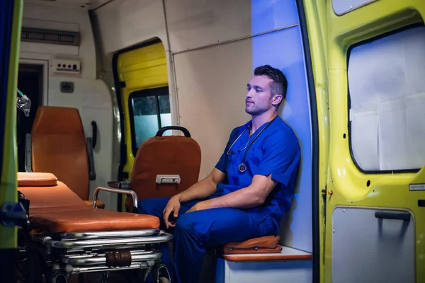 Médico en uniforme médico se sienta con los ojos cerrados dentro del coche ambulancia —  Fotos de Stock