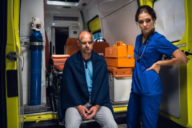 Üniformalı doktor, ambulansta battaniyeli bir adamla duruyor.