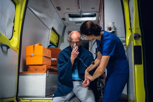 El hombre se sienta en manta con máscara de oxígeno, el médico en uniforme médico sostiene su mano —  Fotos de Stock