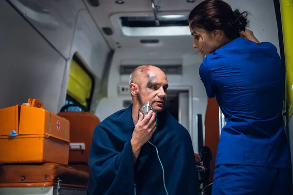 Medico in uniforme medica parla con l'uomo che siede in maschera di ossigeno in coperta — Foto Stock
