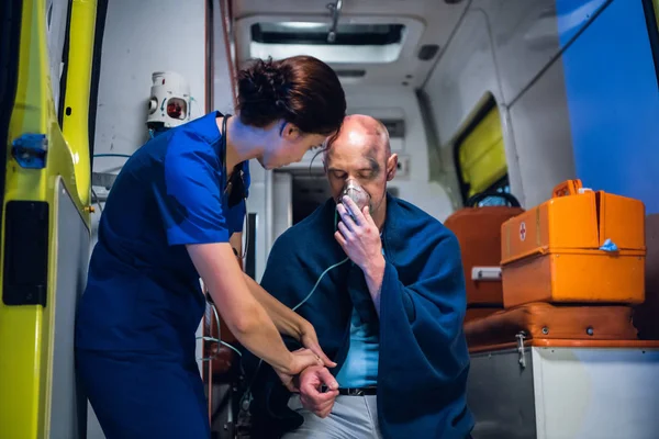 El hombre se sienta con máscara de oxígeno, la enfermera joven en uniforme médico sostiene su mano — Foto de Stock