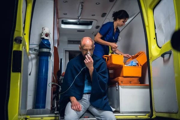 Man breathe through oxygen mask, young nurse packs equipment in medical bag in the ambulance car — Stock Photo, Image