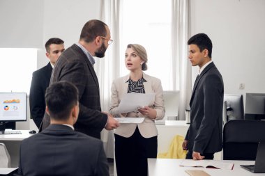 Elinde belgelerle genç bir kadın şefiyle agresif bir şekilde konuşuyor.