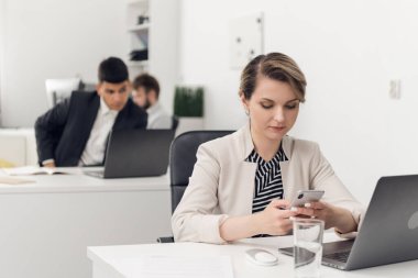 Ofiste çalışan bir kadın telefonunun başında oturuyor.