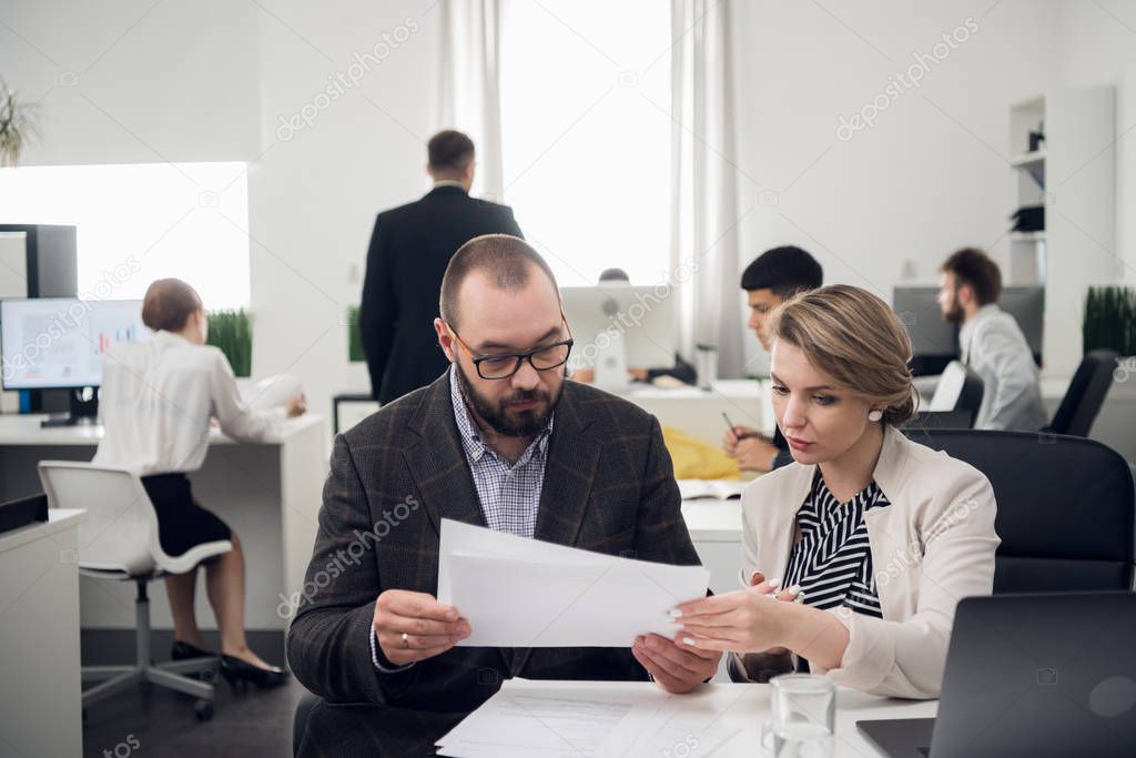 Men and woman in suits discuss something, colleages are busy with work beside them in the office