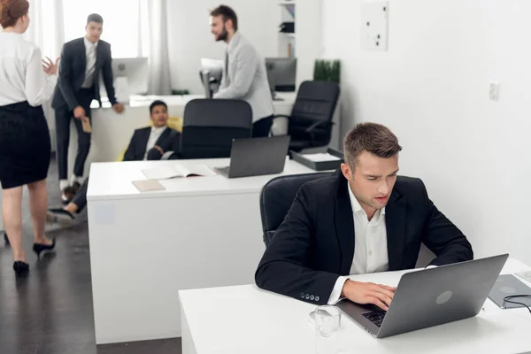Dzień pracy w biurze, młody człowiek siedzi przy stole i pracuje na laptopie w biurze, jego kolekcje stoją obok niego — Zdjęcie stockowe