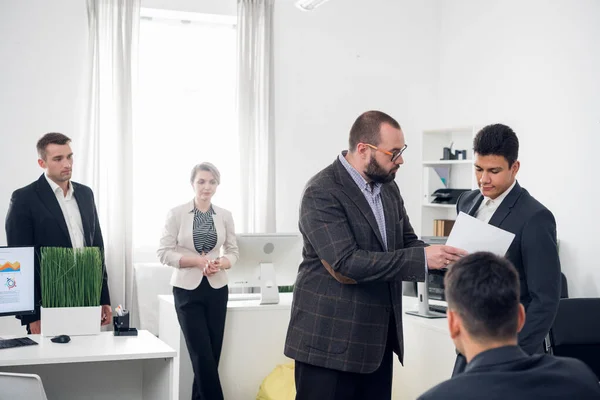 Un día de trabajo en la oficina, el jefe le muestra documentos a un hombre, otros colegas los rodean en la oficina — Foto de Stock