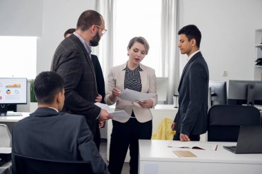 Ofis çalışanları birlikte durur ve belgeleri tartışırlar.