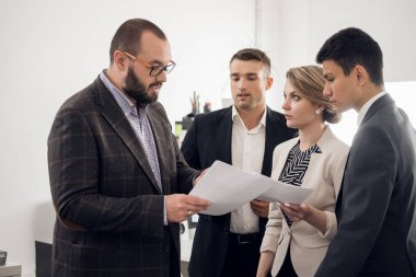 Şef belgeleri gösterir ve meslektaşlarına bir şeyler söyler.